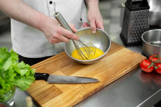 Chef whips eggs with his hands in a bowl to make an omelet with vegetables