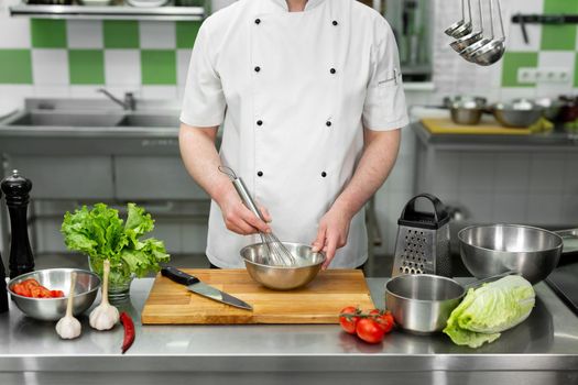 Chef whips eggs with his hands in a bowl to make an omelet with vegetables