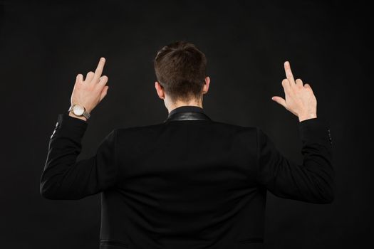 Handsome young man showing middle finger, insult sign on black background