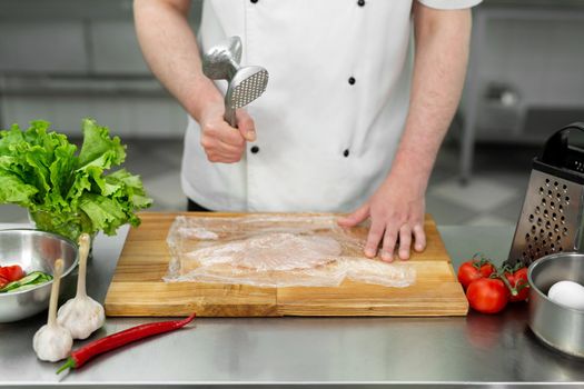 Cook beating a chicken breast with a hammer, close-up. Diet, healthy low-calorie food, weight loss concept