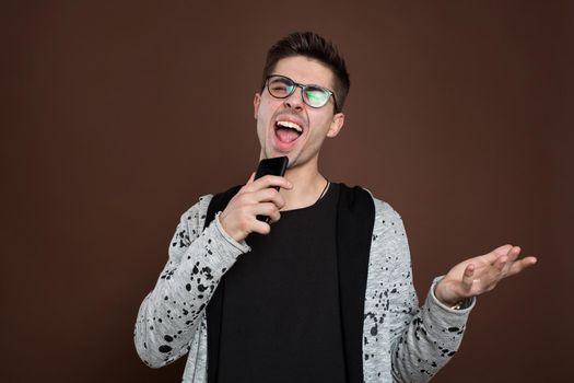 A young man sings into his phone on a brown background