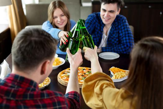 Group of young friends with pizza and bottles of beer celebrate in a cafe.