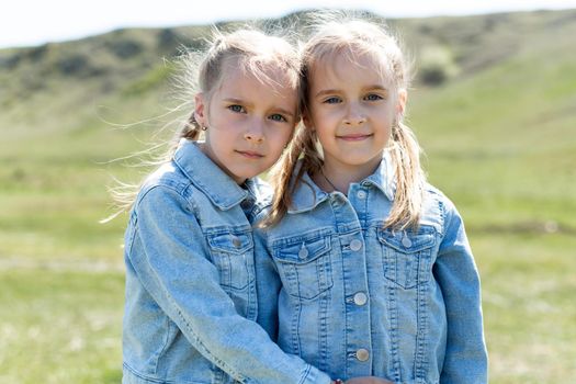 Portrait of two twin sisters who embrace in a meadow in nature.