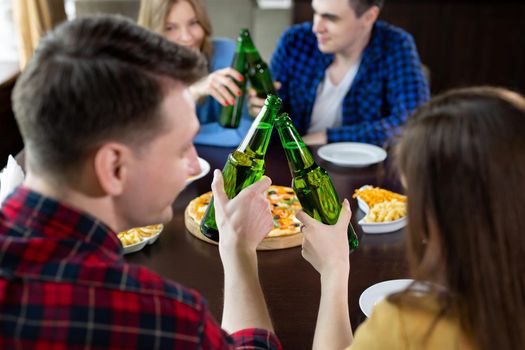 Group of young friends with pizza and bottles of beer celebrate in a cafe.