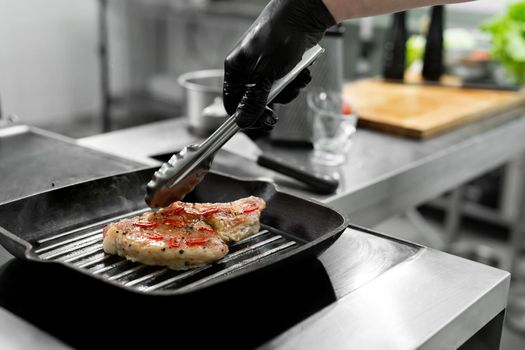 Close-up of a chef's hand holding a grill pan with grilled steaks and vegetables.