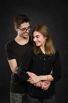 Portrait of young couple in black clothes wearing trendy glasses and posing over black background.