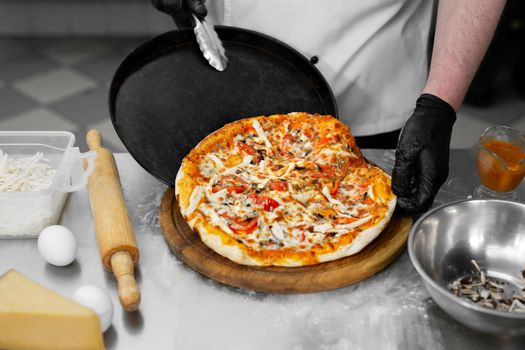 The cook puts the pizza on a wooden Board.