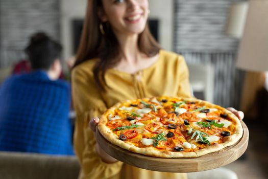 Young beautiful girl poses with a pizza in a cafe against the background of her friends.