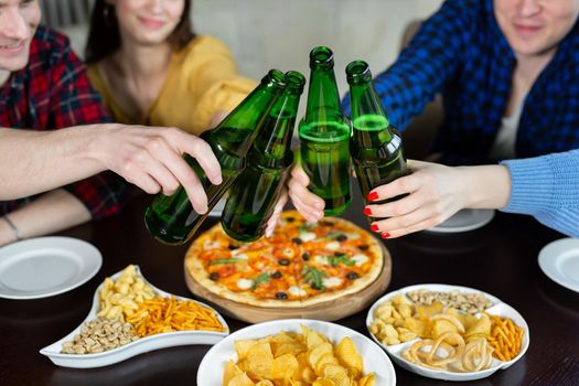 Group of young friends with pizza and bottles of drink celebrating. Close-up of beer bottles and pizza