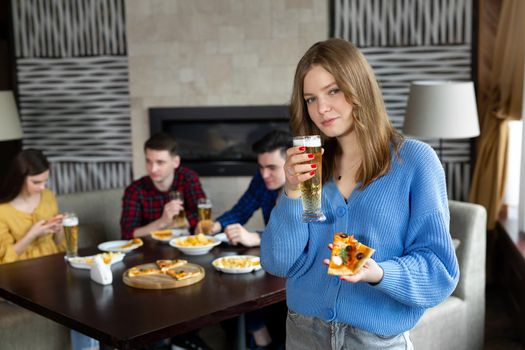 Portrait of a young woman holding pizza and beer in a pub