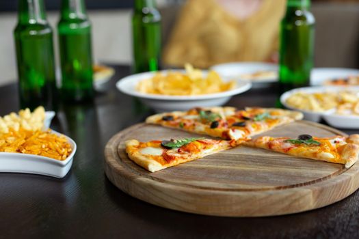 A girl drinks beer while waiting for a friend. Pizza and chips in the foreground