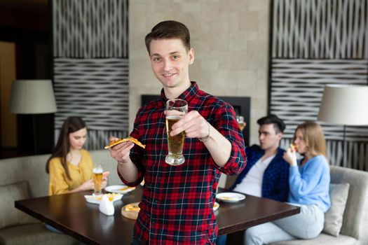 Portrait of a young man holding pizza and beer in a pub