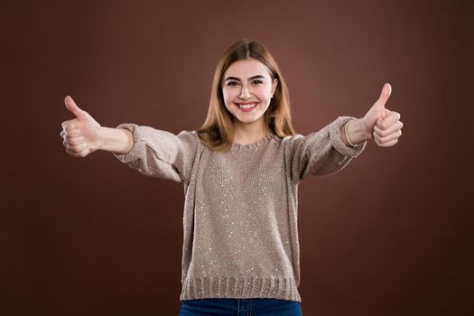 Portrait of trendy young woman showing thumb up over brown background