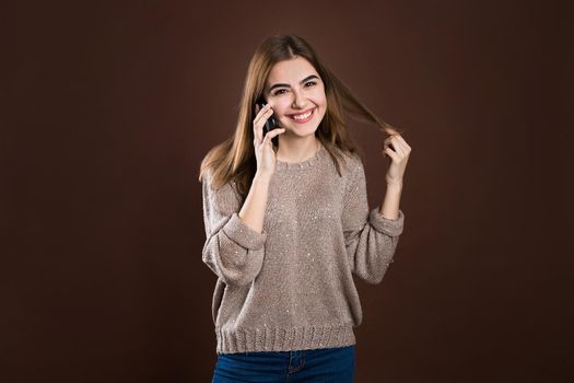 Portrait of a cute happy girl in sweater talking on mobile phone and laughing isolated over sweater background