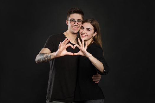 Happy couple in love showing heart with their fingers. Closeup of couple making heart shape with hands.