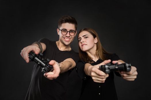Beautiful young couple playing video games with joysticks together, isolated on black background.