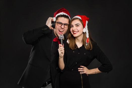 Young couple in love is enjoying a new year's party, putting on Santa hats and headphones, holding a microphone in their hands.