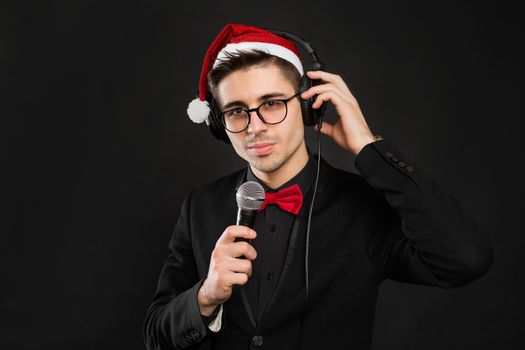 Portrait of a young male showman in glasses and a Santa Claus hat and headphones. With a microphone in his hands at a new year's party