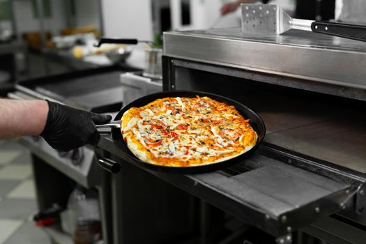 Pizza chef puts pizza in the oven to bake in the oven in the restaurant kitchen