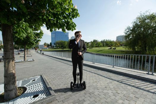 Businessman in a black suit rides a gyro scooter and talks on the phone.