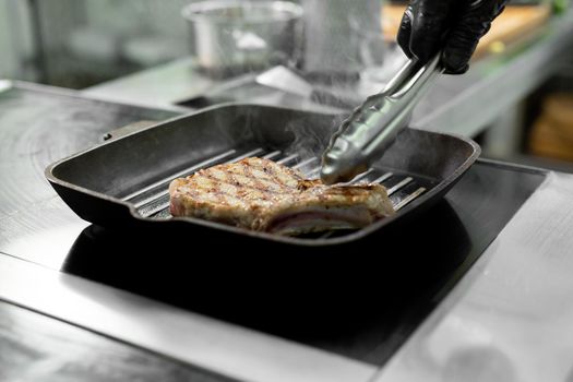 Close-up of a chef's hand holding a grill pan with grilled steaks and vegetables.