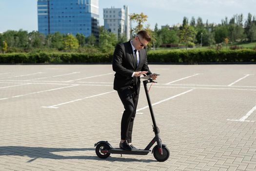 Young handsome businessman in a suit rides an electric scooter and looks at a laptop.