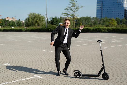 Young handsome businessman in a suit rides an electric scooter around the city and laughs.