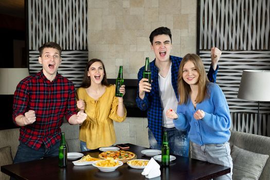 Happy excited joyful four friends watching football on TV in a pub drinking alcoholic drinks eating pizza