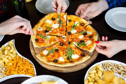 Close-up of handsome young friends drinks beer and eating pizza at pub