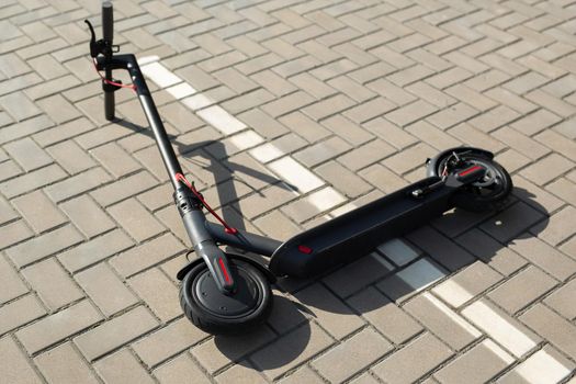 An electric scooter is lying on the sidewalk