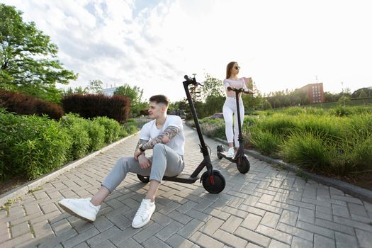 Man and a woman walk on electric scooters in a park