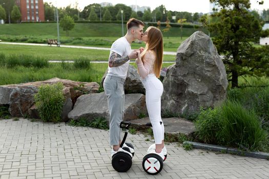 Young man and a woman ride a hoverboard and kiss in the park