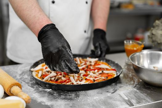 Cooking pizza. Close-up of the cook's hand laying out the meat on the dough.