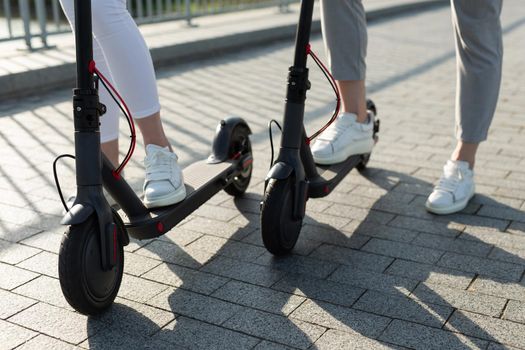 A couple of men and women are walking in the Park and pushing electric scooters.