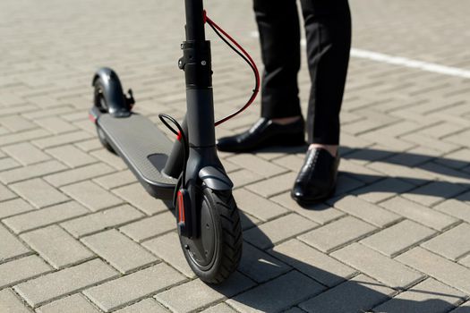 Close-up of a man's feet in a business suit and shoes near an electric scooter.