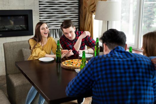 Group of young friends with pizza and bottles of drink celebrate in a cafe