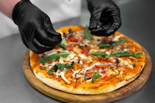 Close-up of the chef's gloved hands decorating pizza with greens, arugula.