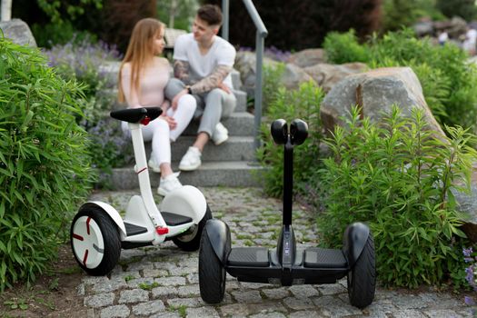 Young man and a woman kiss in the park. In the foreground hoverboard