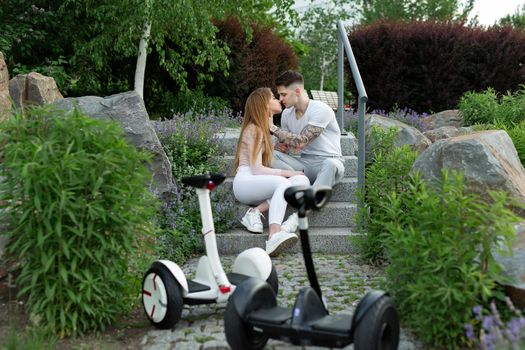 Young man and a woman kiss in the park. In the foreground hoverboard