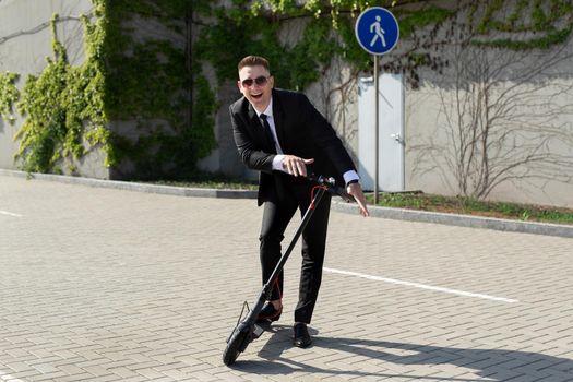 Man in a business suit is having fun and laughing near an electric scooter.