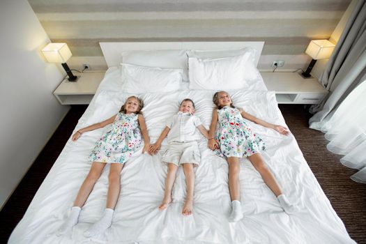Twin sisters and a brother lie on a bed in a hotel room