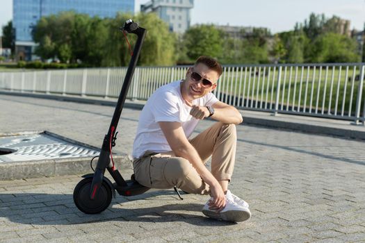 Cheerful man is sitting on an electric scooter in a park
