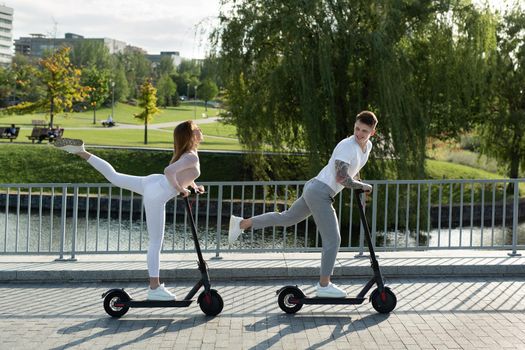 Young couple on vacation having fun driving electric scooter through the park