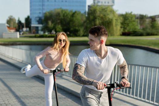 Beautiful young couple is enjoying sunny summer day while riding their own electro scooters.