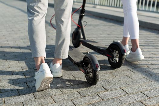 A couple of men and women are walking in the Park and pushing electric scooters.