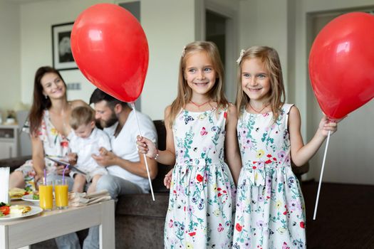 Two twin sisters pose with balloons in the background of the family. who eats breakfast in a hotel room.
