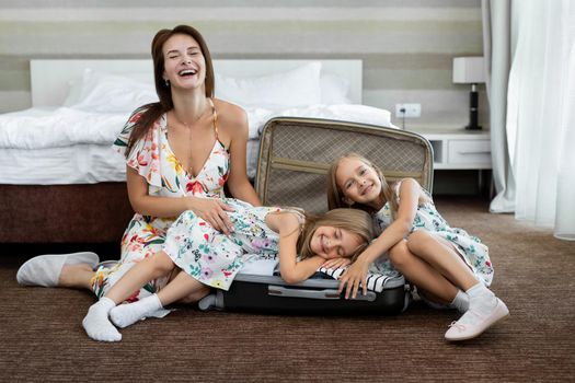 Young mother and her twin daughters with a suitcase in a hotel room.