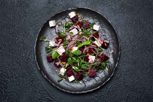 Salad of microgrin, beetroot and cheese with fresh onions and seeds on a plate on a black background. top view.