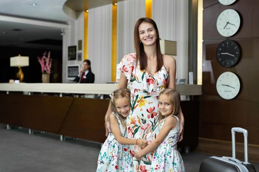 Mother with twin daughters hugging at the hotel reception.