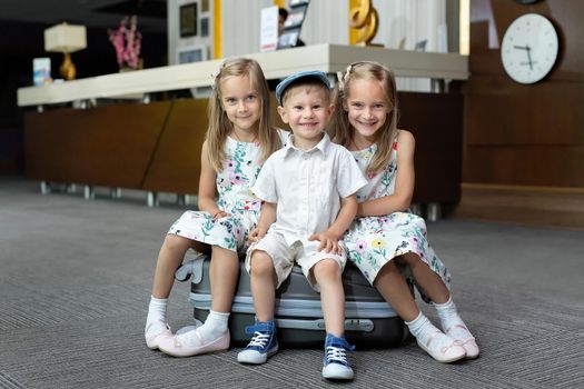 Twin sisters and brother sitting on a suitcase in a hotel.